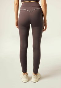 Leggings in dark purple fabric, featuring a high waistband and white piping detail along the back. Smooth texture, fitted design.