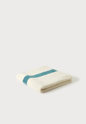 Serviette blanche pliée avec une seule bande horizontale bleu sarcelle sur un fond blanc uni.