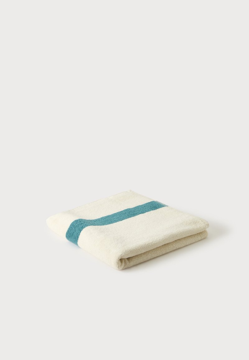 Serviette blanche pliée avec une seule bande horizontale bleu sarcelle sur un fond blanc uni.