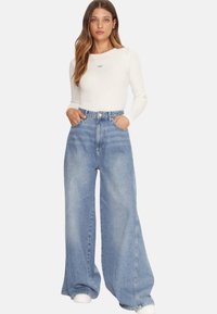 Top bianco leggero a maniche lunghe abbinato a jeans azzurri a vita alta e a gamba larga; presenta tasche e una vestibilità comoda.