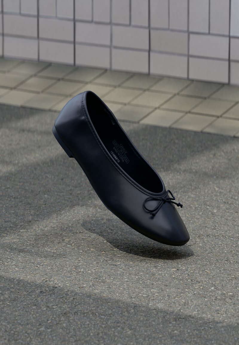 Μαύρο δερμάτινο μπαλαρίνα με μικρή λεπτομέρεια φιόγκου, αιωρούμενο πάνω από επιφάνεια από άσφαλτο κοντά σε πλακιδωτό τοίχο.