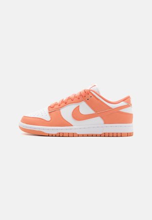 Nike Dunk Low-sneakers har en vit läderöverdel med korallfärgade mockadetaljer, platta snören, gummisula och den karakteristiska swoosh-logotypen.