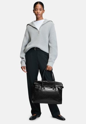 Schwarze Lederhandtasche mit strukturierter Form und doppelten Griffen, kombiniert mit einem strukturierten grauen Pullover und dunklen Hosen.