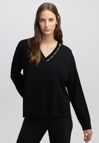 Schwarzer V-Ausschnitt-Pullover mit langen Ärmeln, mit einem kleinen Ausschnitt am Hals, geschmückt mit Metallakzenten. Weiches Strickmaterial, entspannte Passform.