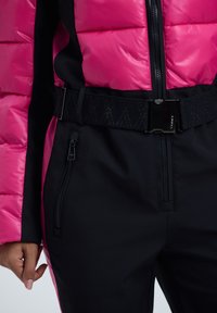 Chaqueta de invierno con bloque de color, parte superior de plumón rosa y parte inferior negra. Cuenta con un cinturón ajustable negro y un bolsillo con cremallera en el costado.