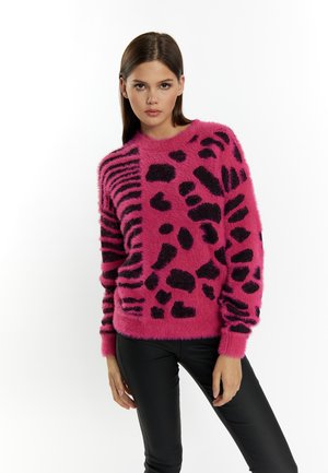 Pulover pufos roz cu modele de imprimeu animal negru, cu guler rotund și mâneci lungi, purtat peste pantaloni negri strâmți.