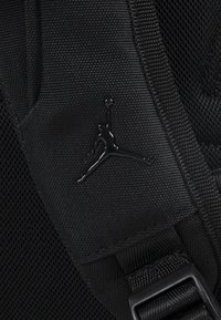 Fekete szövet hátizsák hálós panelekkel, fényes fekete Jordan logóval és masszív, szabályozható műanyag csatokkal ellátott heveder pántokkal.