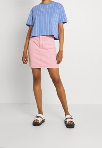 Blårandig kortärmad skjorta, rosa denimkjol och vita sandaler med svarta sulor. Outfitten har en avslappnad passform och enkel design.