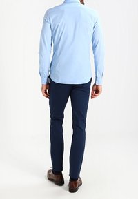 Ljusblå långärmad skjorta med knäppta manschetter, matchad med mörkblå slim fit-byxor och bruna skor. Ren, skräddarsydd design.