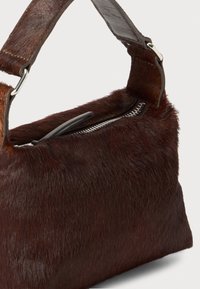 Borsa in pelliccia marrone con una tracolla in pelle liscia. Presenta una chiusura con zip lungo la parte superiore e una superficie morbida e texture.