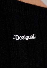 Black knitted sweater features a ribbed texture and a silver logo tag with "Desigual" in a modern font. The fabric is soft and thick.