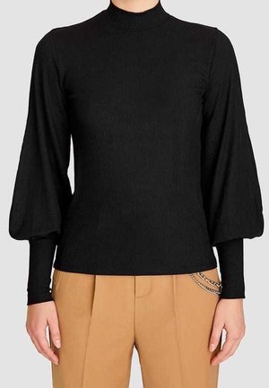 Haut noir côtelé à manches longues avec manches supérieures bouffantes et manches inférieures ajustées, porté avec un pantalon beige avec un accessoire chaîne argentée.