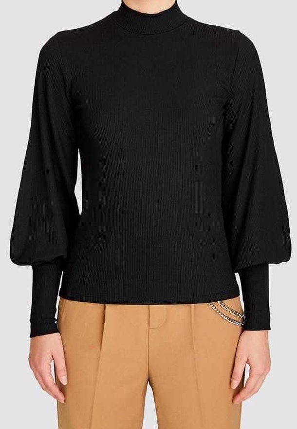 Haut noir côtelé à manches longues avec manches supérieures bouffantes et manches inférieures ajustées, porté avec un pantalon beige avec un accessoire chaîne argentée.