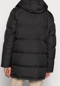 Svart pufferjacka med huva, kviltad design och elastiska ärmslut. Tillverkad av ett smooth, vattenavvisande material.