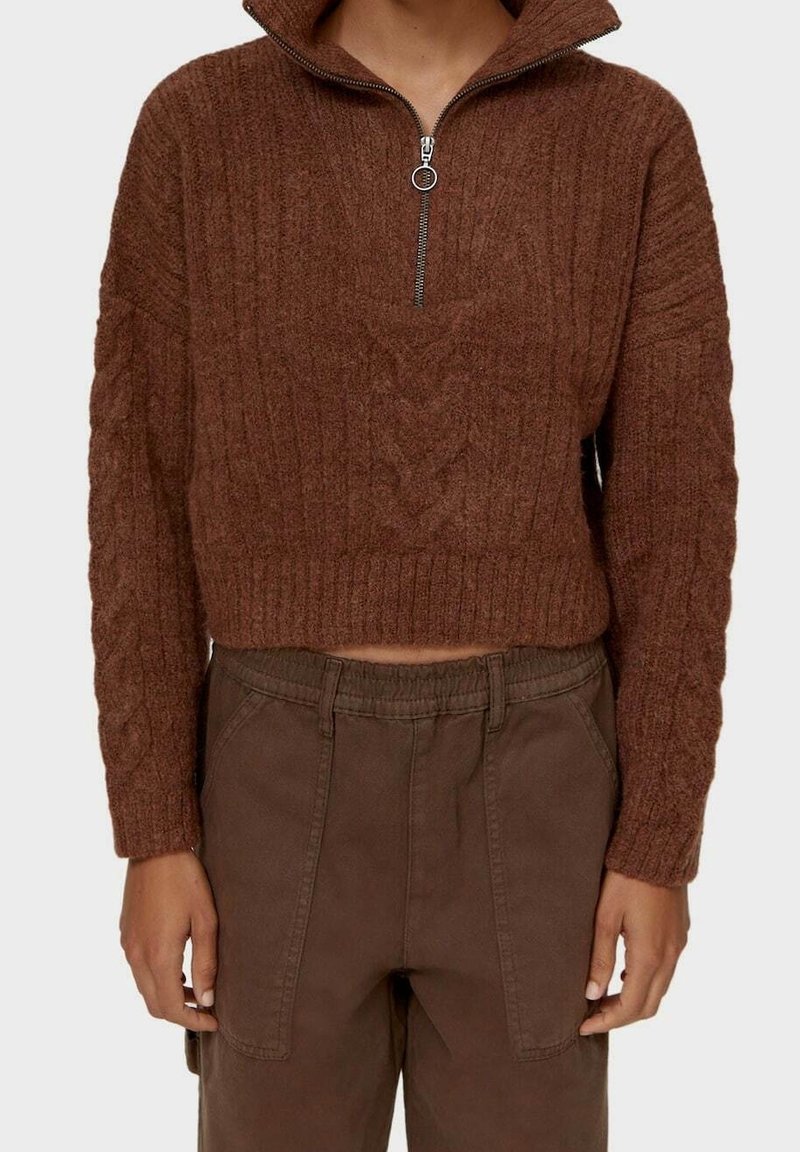 Pull court en maille torsadée marron avec col à demi-fermeture éclair et pantalon marron taille haute avec poches plaquées à l'avant.