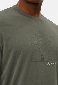 T-shirt en coton vert olive avec un graphique minimaliste de montagne et de sentier. Nom de la marque "VAUDE" affiché dans le coin inférieur droit.