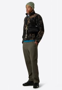 Fleece jacket in black and brown leopard print, teal shirt underneath, olive pants, black crossbody bag, green beanie, black shoes.