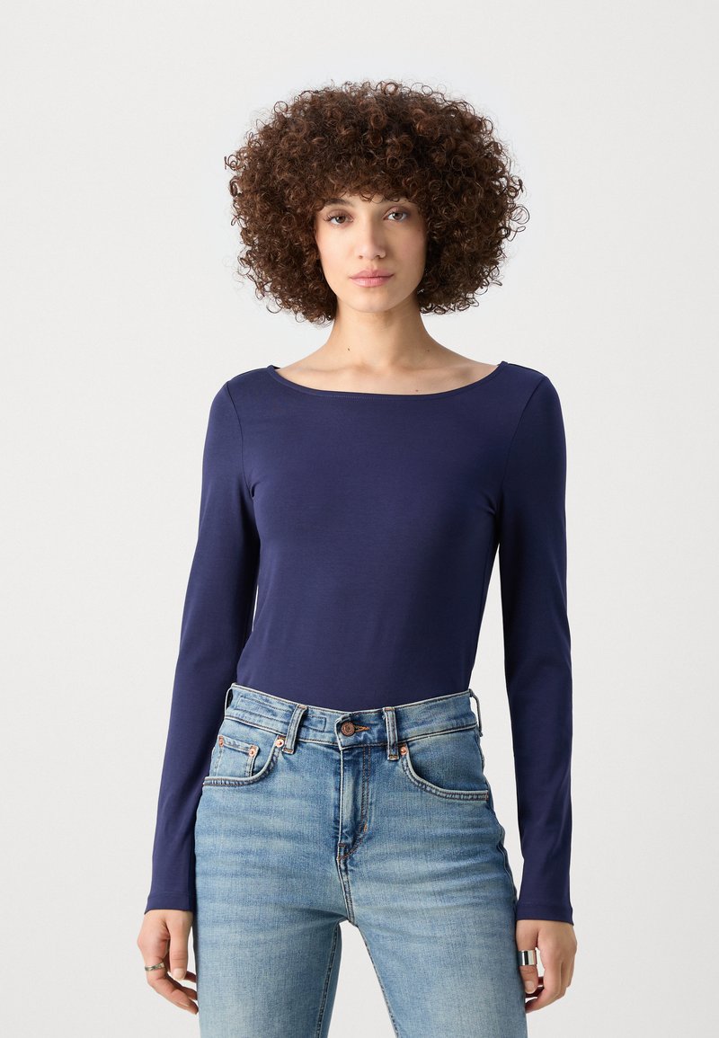 Haut à manches longues bleu marine en tissu lisse et extensible avec un col large, associé à un jean taille haute bleu clair avec une fermeture à bouton.
