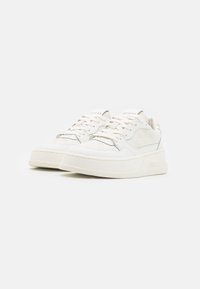 Baskets blanches en cuir et mesh, avec une semelle plate, un bout rond, et un détail de logo embossé sur le côté et la languette.