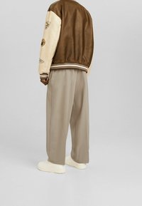 Chaqueta bomber de cuero marrón y crema con parches, puños acanalados, combinada con pantalones de pierna ancha beige y zapatillas blancas. 