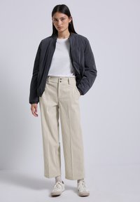 Grijze bomberjack, witte t-shirt, beige wijde corduroy broek, en lichte sneakers. Eenvoudig ontwerp met minimale hardwaredetails.