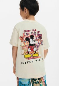 Bež majica od pamuka s grafikom Mickey Mousa i tekstom "Žao mi je zbog mog lošeg raspoloženja." Kratki rukavi i standardni kroj, prikazano stražnje gledište.