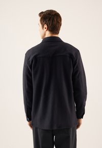 Veste en polaire bleue marine avec un col, des manches longues et une coupe droite. Elle présente un tissu texturé et des poignets à boutons.