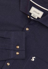 Námornícky modrá košeľa na gombíky vyrobená z textúrovanej látky, s zlatými gombíkmi, kontrastným prešívaním a malým vyšitým logom zajaca.