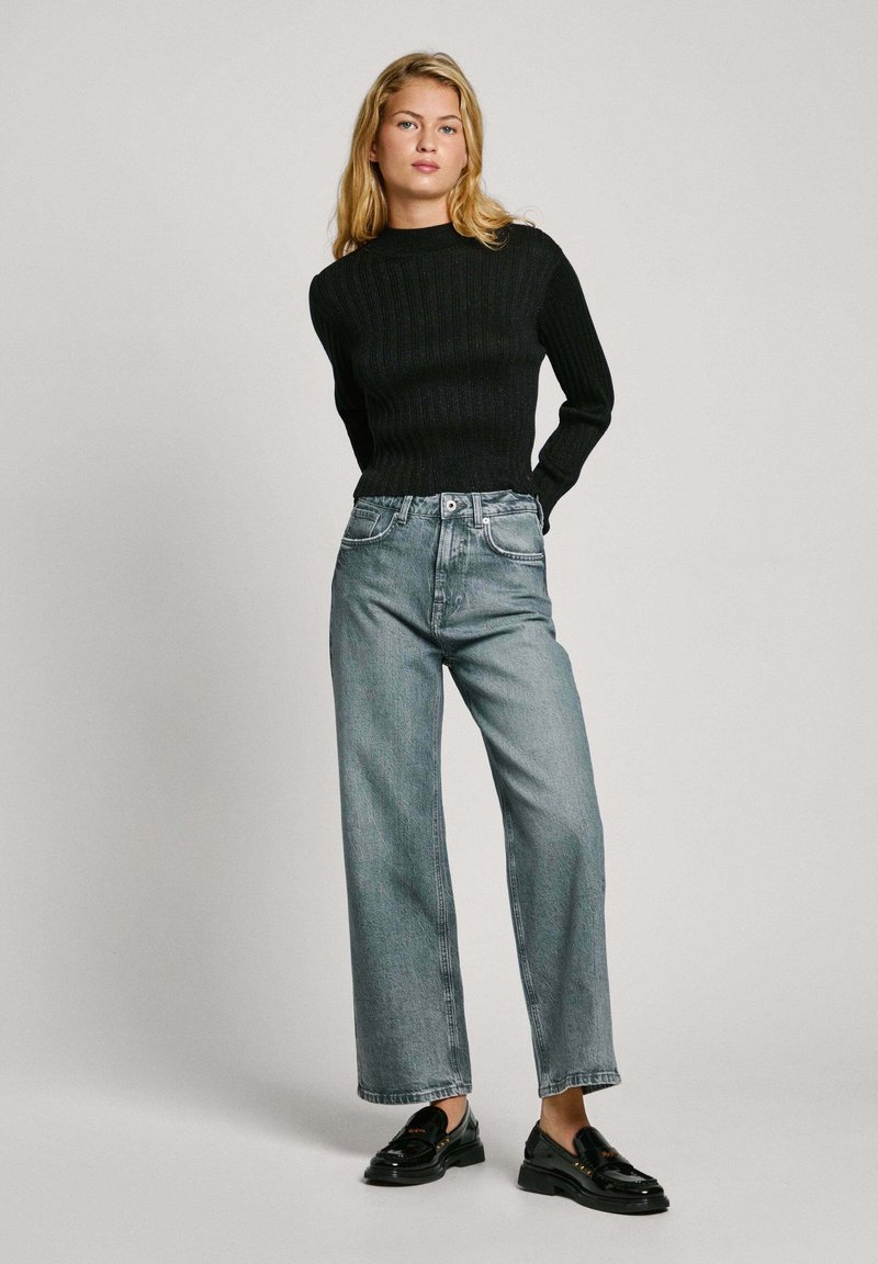 Maglione nero a coste abbinato a jeans in denim azzurro chiaro a vita alta e pantaloni larghi, completato da mocassini neri, con una vestibilità rilassata e design a cinque tasche.