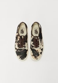 Black and white spotted sneakers with a soft, textured surface, brown laces, and a cream rubber sole. Features Vans logo on insoles.