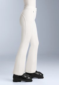 Pantaloni de schi ajustați, albi, cu o textură netedă, având cusături laterale și talie înaltă. Asortați cu bocanci de schi negri, cu bucle ajustabile.