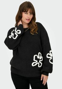 Zwarte gebreide trui met een wit decoratief bloemmotief op de mouwen. Heeft een losse pasvorm en een gestructureerde stof.
