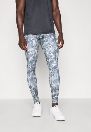 Heren camouflage leggings van rekbaar materiaal, met grijs en blauw in een digitaal patroon. Gecombineerd met witte sneakers en een zwart shirt.