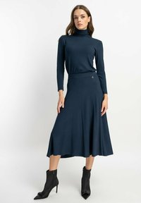 Langärmliges Rollkragenkleid in Dunkelblau, aus weichem Stoff gefertigt. Schwingendes Rockdesign, knielang, kombiniert mit eleganten schwarzen Stiefeletten.