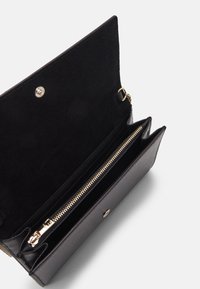 Czarny skórzany portfel z zapinaną na zamek przegrodą, podszewką z zamszu, miejscami na karty i złotymi elementami ozdobnymi, zamykany na zatrzask.