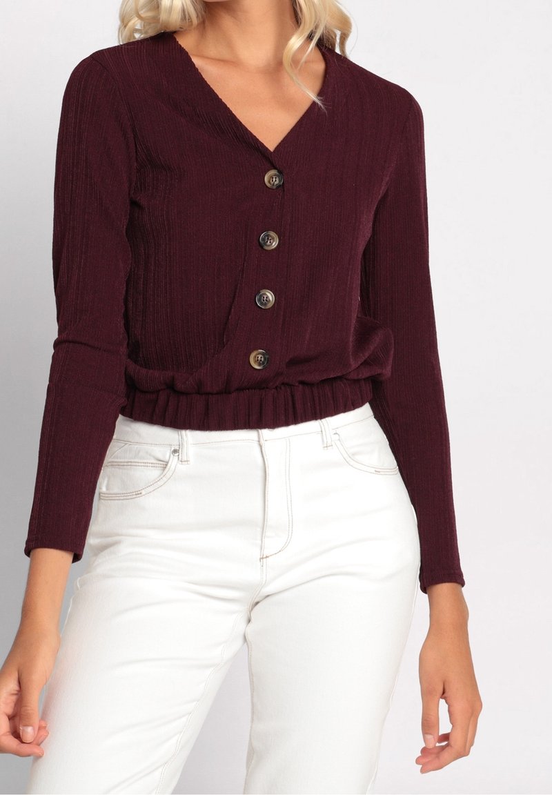 Haut en tricot côtelé bordeaux avec un décolleté en V, des manches longues et une taille cintrée, doté de cinq boutons sur le devant et d'une finition texturée.