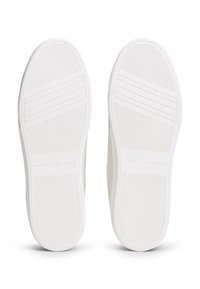 Semelles blanches en caoutchouc d'une paire de chaussures décontractées avec des motifs de traction texturés et la marque "Tommy Hilfiger" embossée au centre.