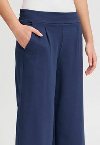 Pantalons larges bleu marine avec une texture douce, dotés de plis et d'une ceinture côtelée. Comprend une poche latérale pour plus de praticité.