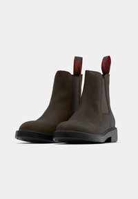 Rjavi usnjeni gležnarji z elastičnimi stranskimi paneli, zaobljenim prstom in črnim gumijastim podplatom. Imajo rdeče trakove za lažje obuvanje z znamko.