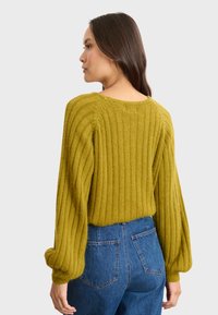 Sweter w kolorze oliwkowej zieleni, pleciony w prążki, z balonowymi rękawami, okrągłym dekoltem i luźnym krojem, zestawiony z dżinsami o wysokim stanie w niebieskim kolorze.