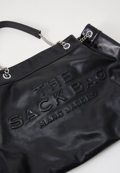 Mustat nahkainen käsilaukku, jossa on kohotettua tekstiä "THE SACK BAG" ja "MARC JACOBS." Varustettu ketjuyksityiskohdalla ja litteällä kahvalla. Liukas pinta.