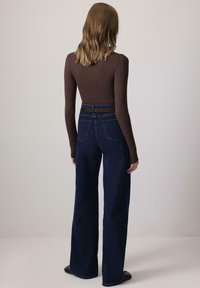 Hnedý top s dlhým rukávom spárovaný s vysokými, širokými tmavomodrými džínsami. Tento outfit má priliehavý strih a minimálne detaily.