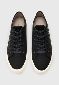 Sneakers neri in canvas con punta rotonda, suola piatta bianca e lacci neri. Presentano la scritta "ALLSAINTS" stampata di lato in grigio scuro.