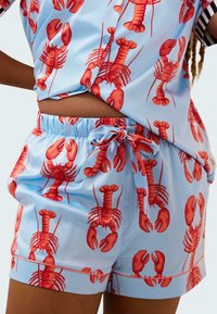 Conjunto de camisa azul de manga corta y pantalones cortos con un estampado de langosta en rojo. Los pantalones cortos tienen una cintura elástica con cordón.