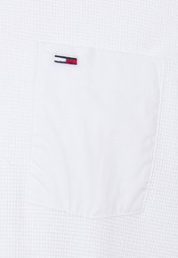 Weißer, strukturierten Stoff mit einer quadratischen Tasche. Die Tasche zeigt ein kleines Logo mit einem Rot-, Weiß- und Blaustreifen-Design.
