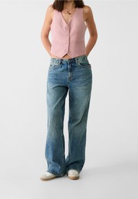 Světle růžová bezrukávová vesta s pěti knoflíky, spárovaná s širokými modrými džínami. Vzhled dokončují pohodlné bílé tenisky.