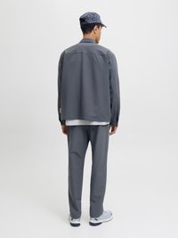 Hall olnud hall ülikond ja püksid, mõlemad sujuva tekstuuriga. Modell kannab mustriga mütsi ja heledat värvi spordijalatu. Taust on puhas valge.