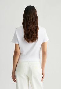 Hvid bomulds t-shirt med korte ærmer og cropped design, parret med lyse jeans med baglommer og et syet mærke.