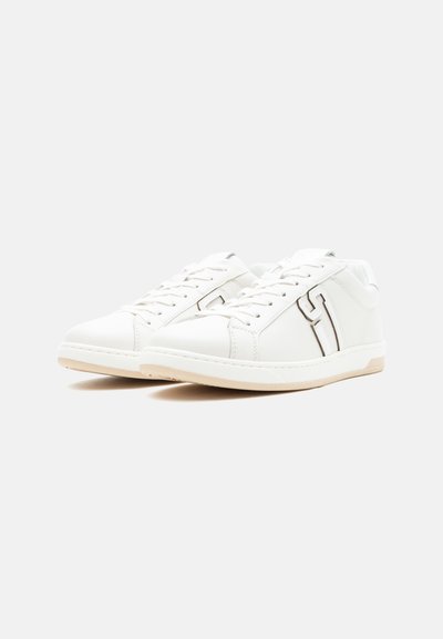 Baskets en cuir blanches à tige basse avec semelles beiges et lacets blancs, présentant un détail de couture sur le côté en forme de "T".