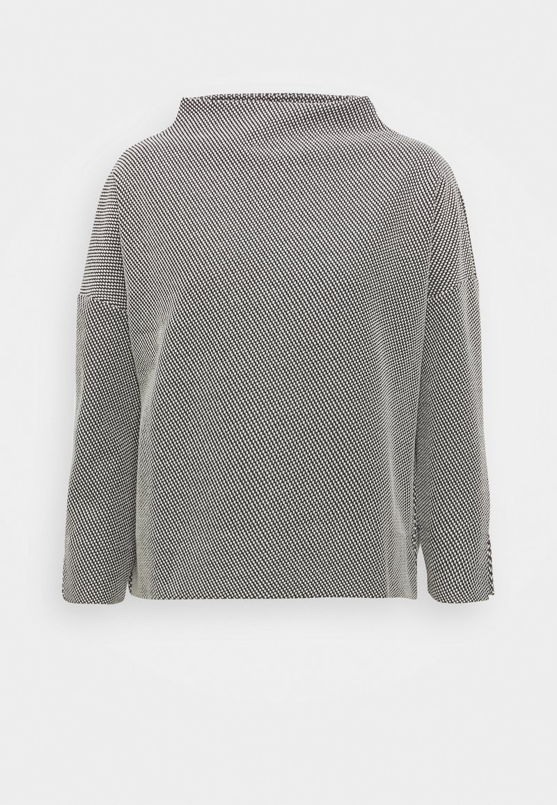 Haut à manches longues à motifs noirs et blancs avec un col rond haut et une coupe ample sur fond blanc uni.
